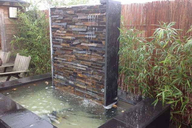 modern waterelement van muurstrips. het waterelement is 180 cm hoog en 120cm breed, onder een waterbak spiegelvijver met waterplanten